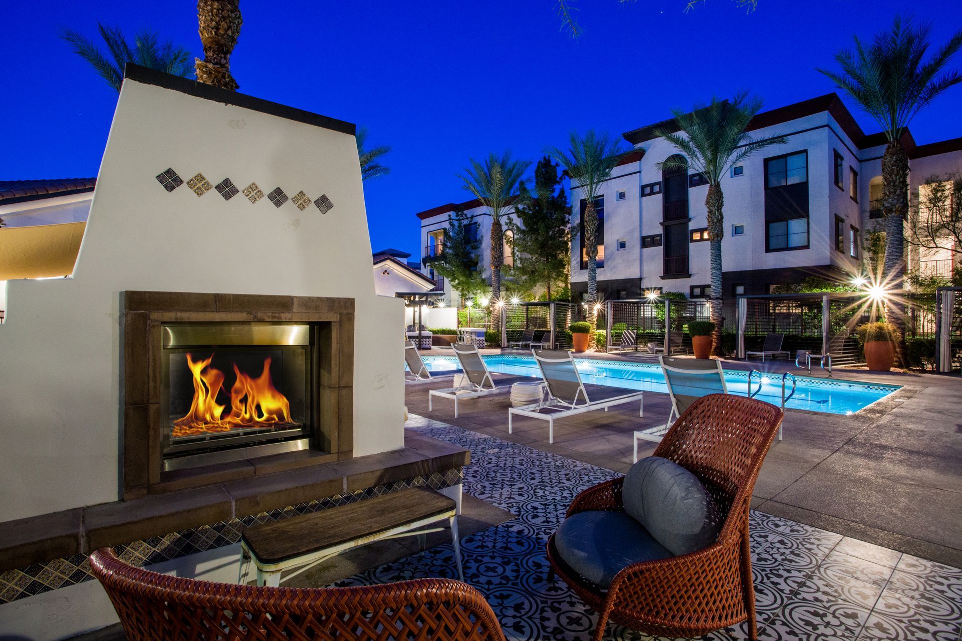Poolside patio with lit fireplace, lounge chairs, and modern apartment buildings at dusk — Las Vegas commercial multi-family property photography