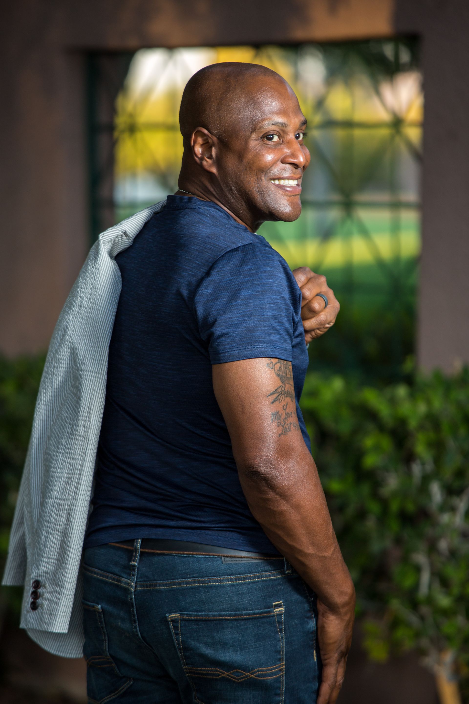 Person in a navy shirt and jeans looks back over their shoulder outdoors, holding a gray jacket — Las Vegas portrait photography