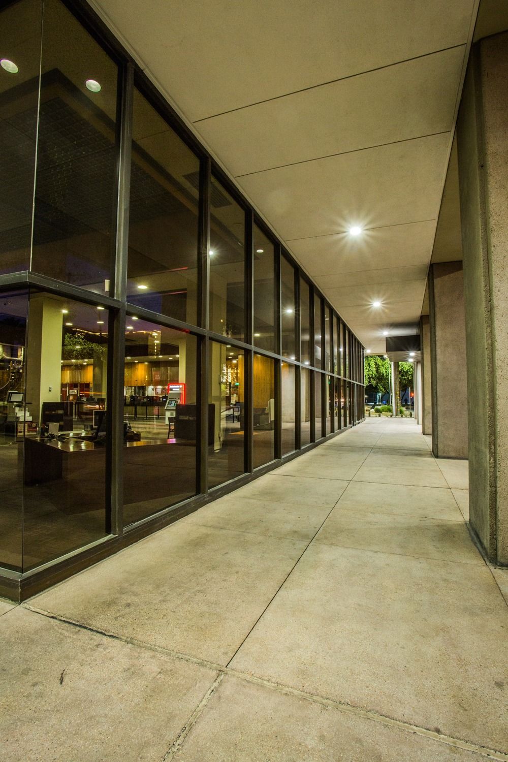 Empty covered sidewalk beside glass storefronts at night, lit by overhead lights — Las Vegas architectural photography