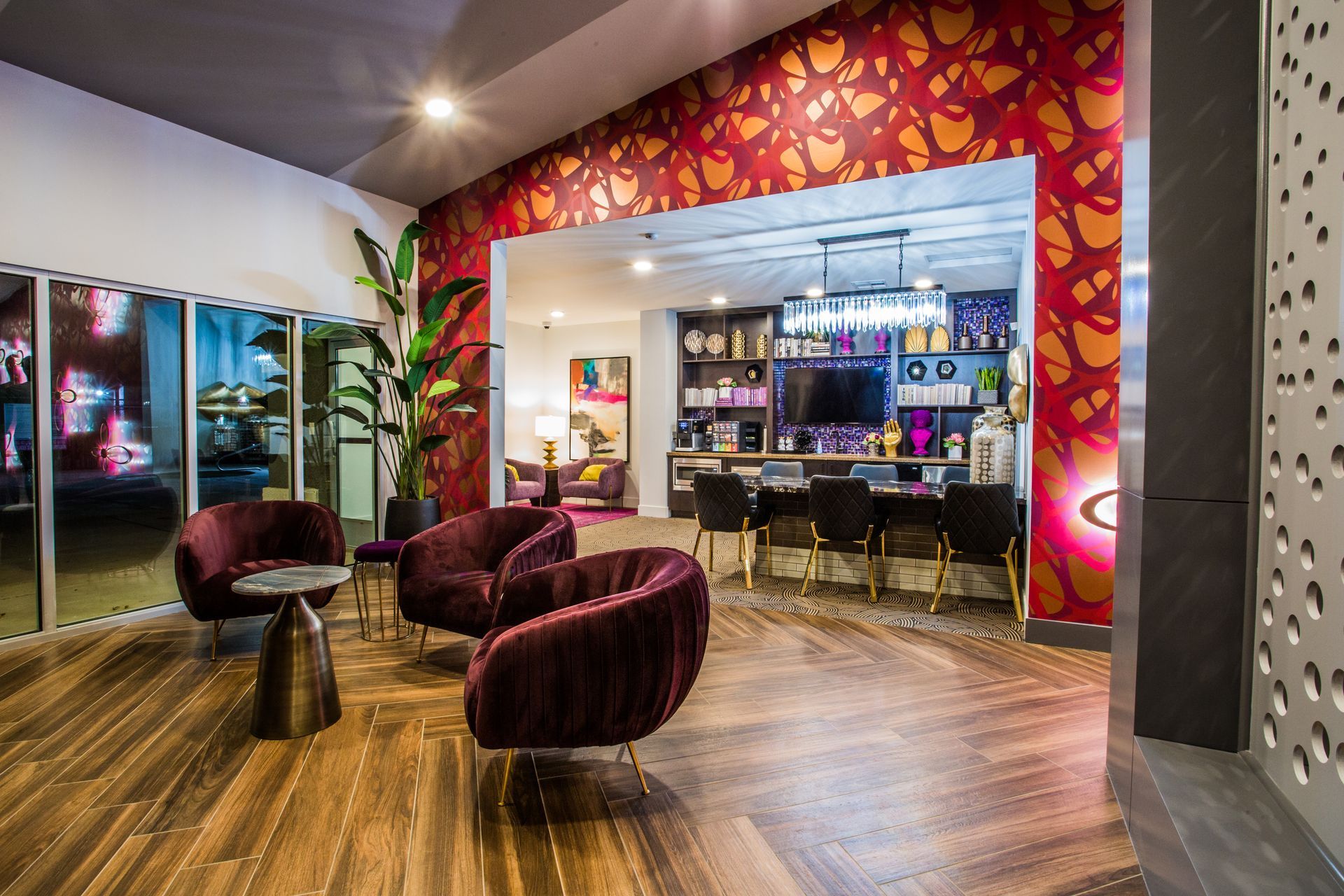 Modern salon lounge with burgundy chairs, wood floor, colorful patterned wall, and reception counter in back — commercial multi-family property photography