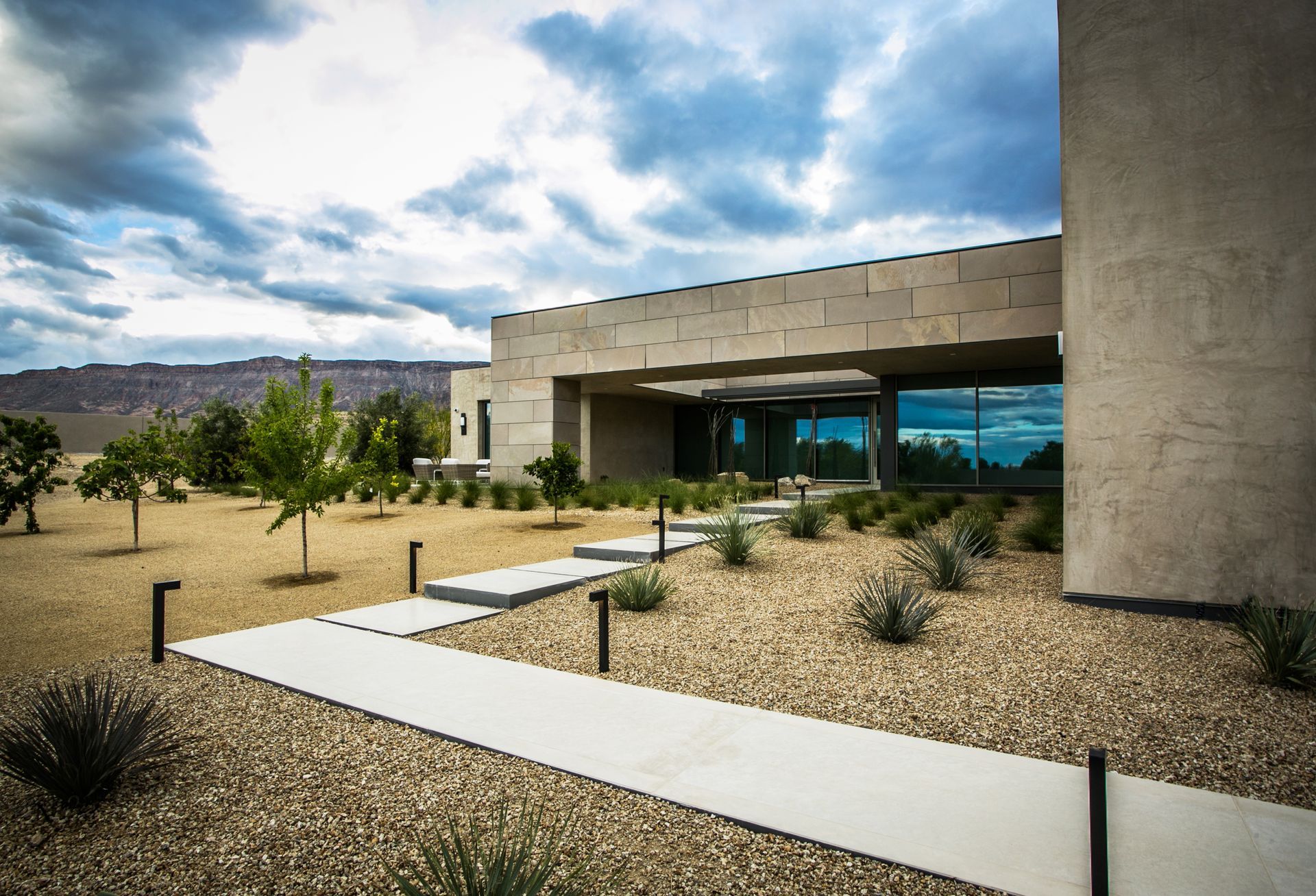 Modern concrete house with desert landscaping under a cloudy sky — real estate photography