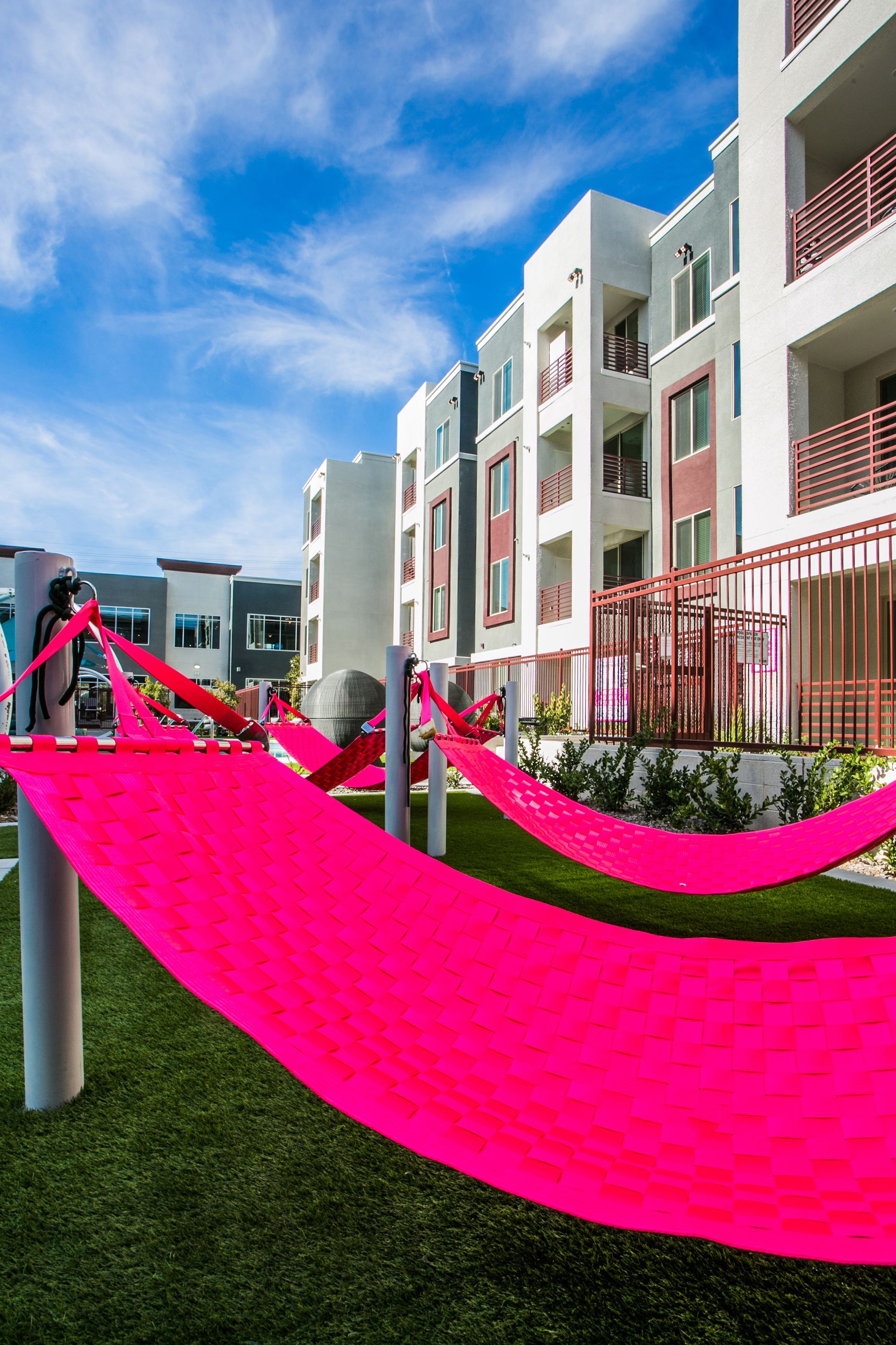 Bright pink fabric hammocks on a grassy courtyard beside modern white — multi-family photography