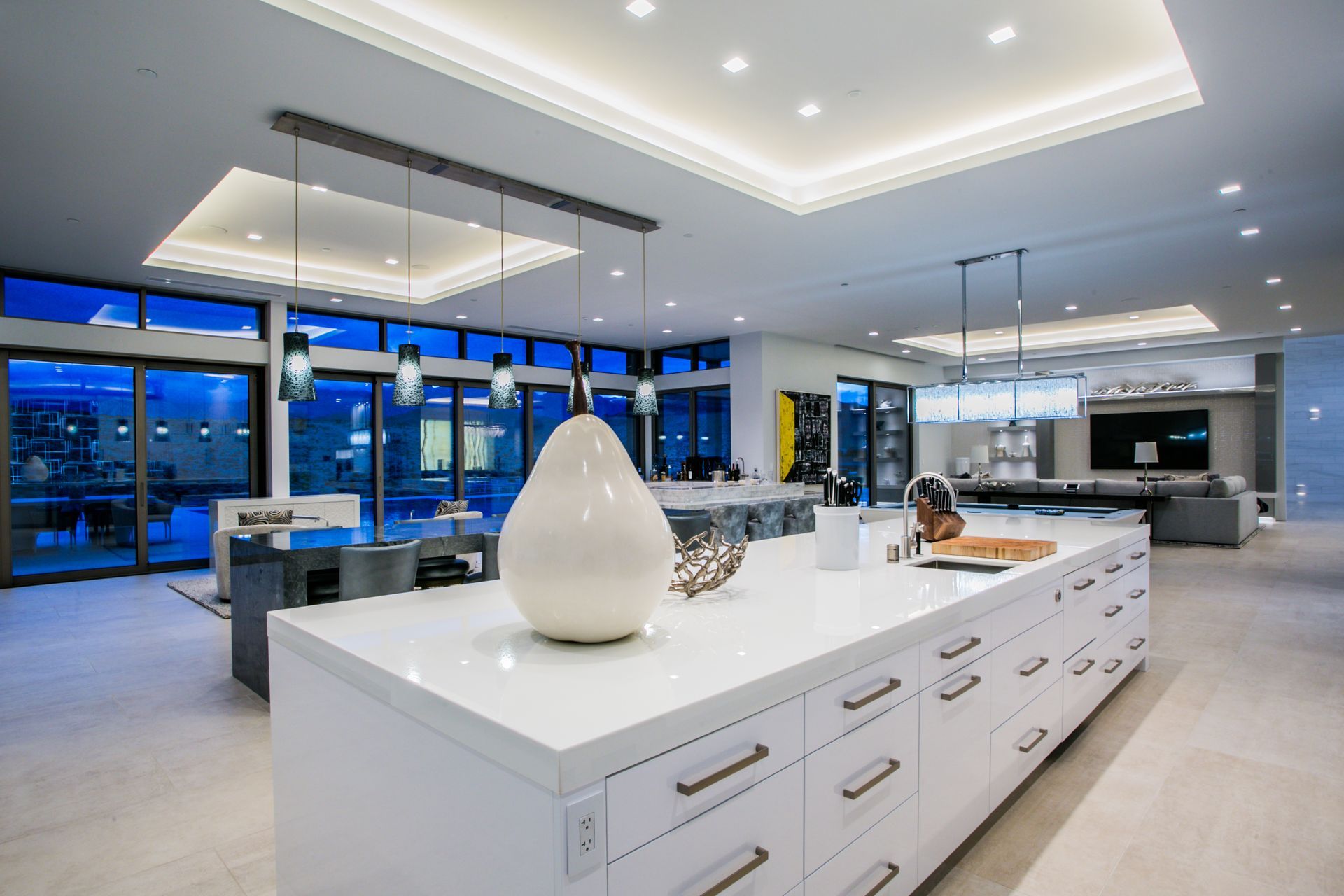 Modern luxury kitchen with white island, pendant lights, and open living area at dusk — Las Vegas real estate photography