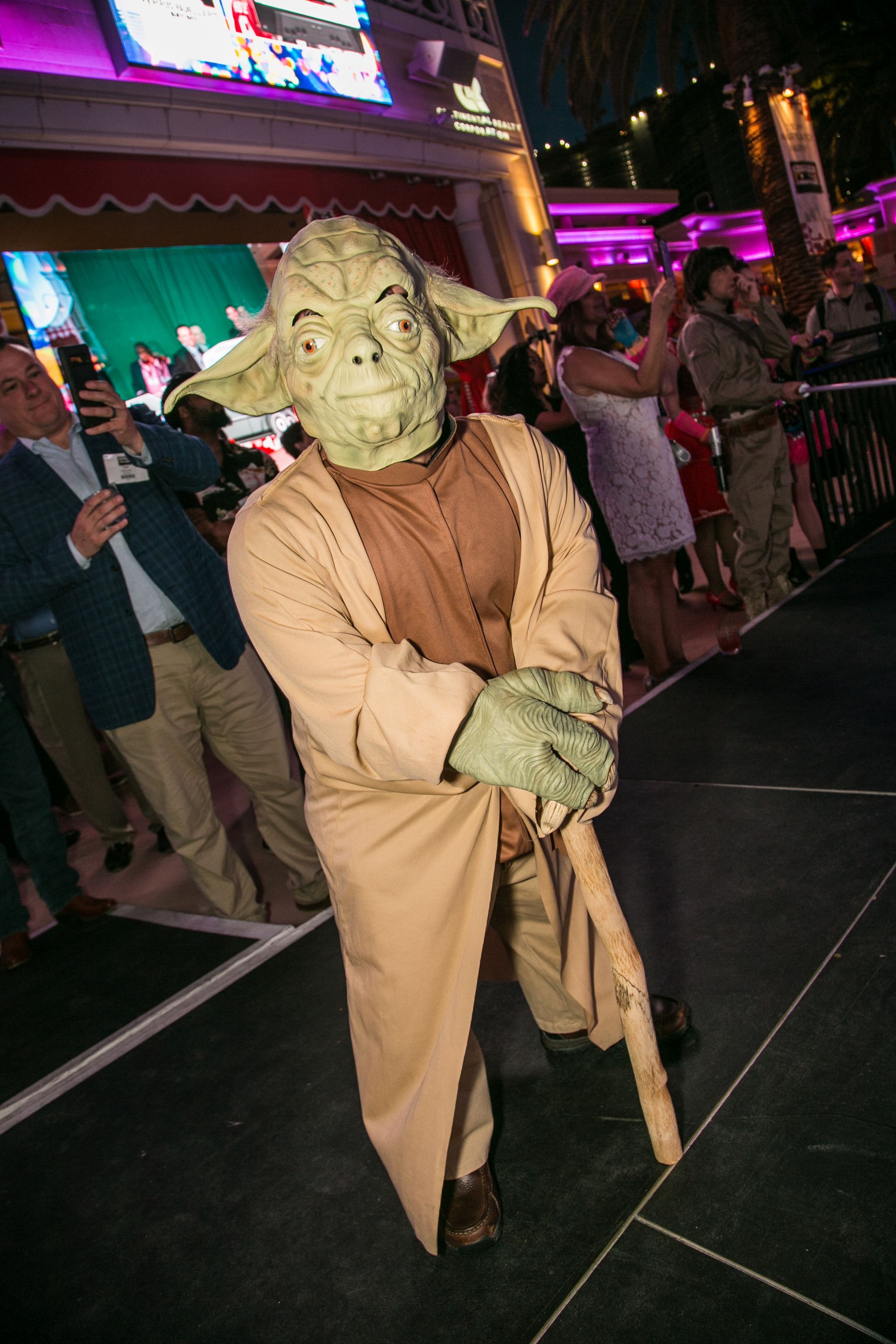 Yoda costume at a nighttime event, holding a cane and standing on a lit street