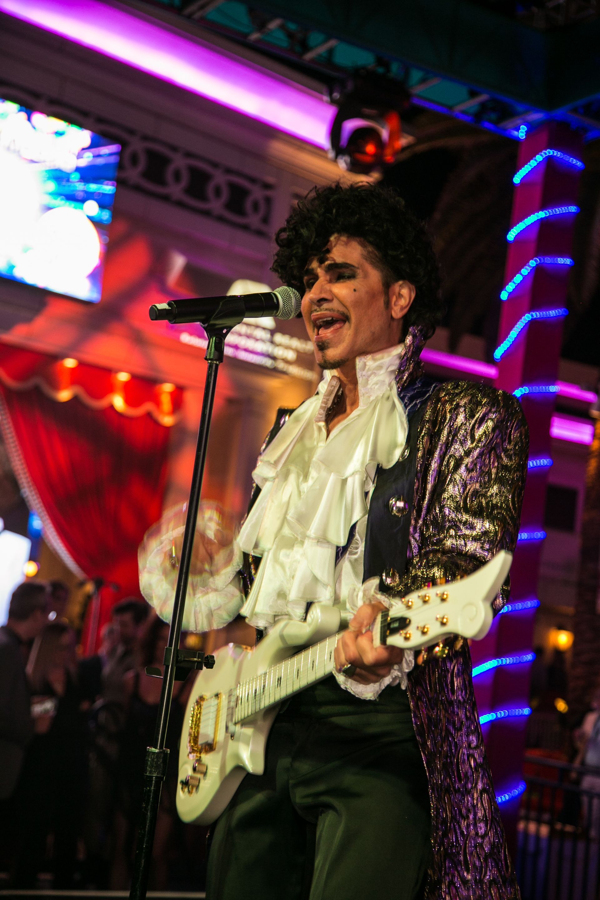 Musician singing and playing electric guitar on a colorful stage with purple — event photography