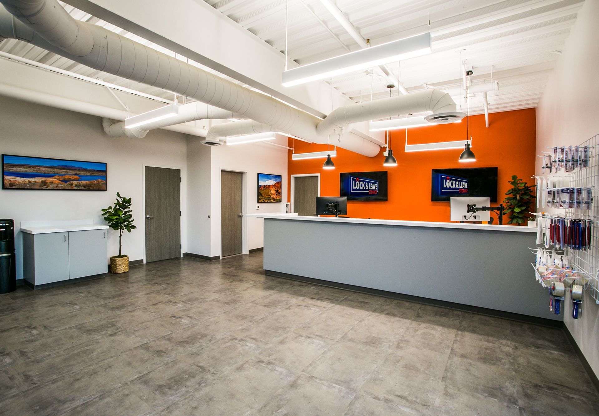 Modern office reception area with a gray desk, orange accent wall, and white industrial ceiling — commercial multi-family property photography