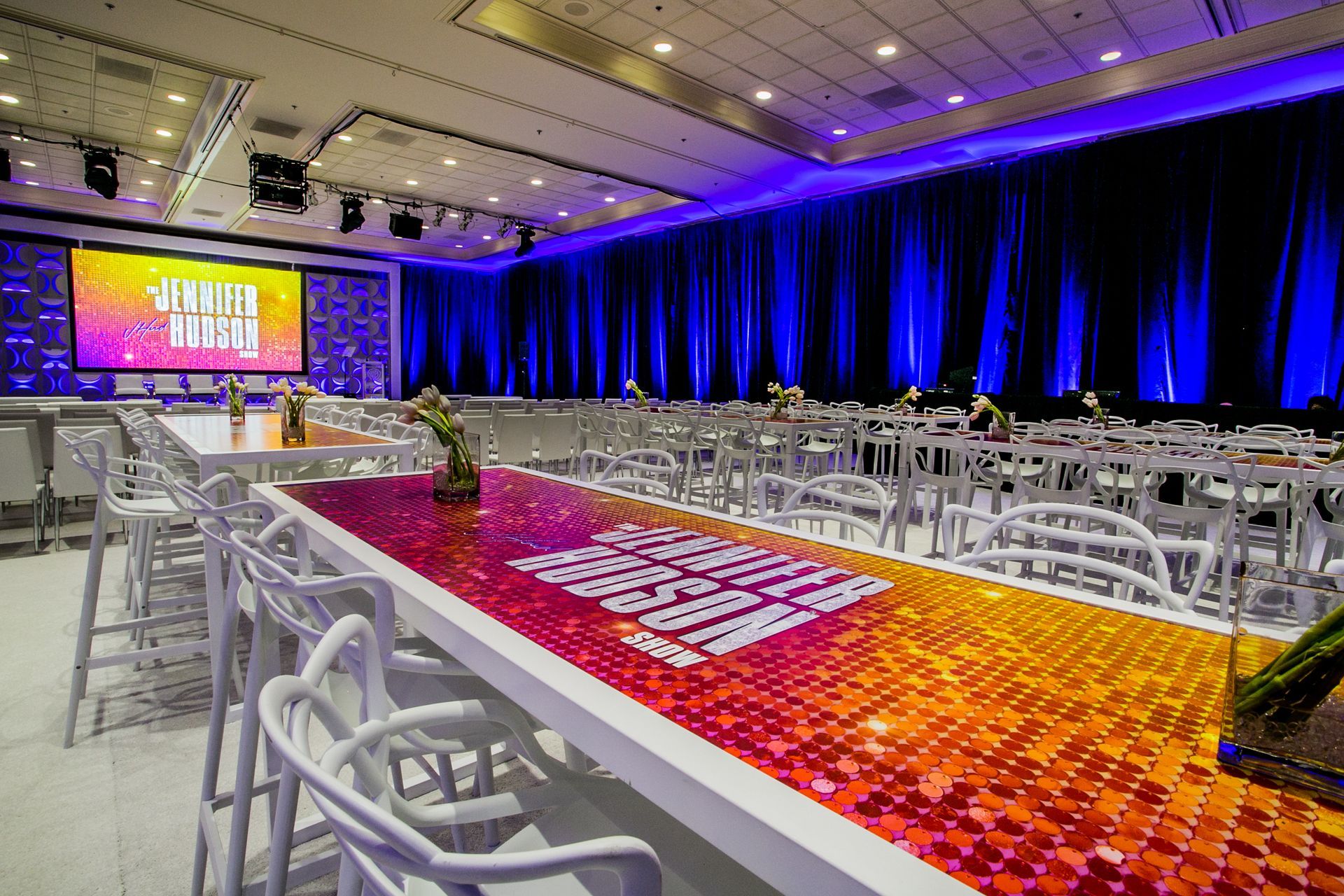 Conference hall with rows of white chairs, a lit stage screen — multi-family photography