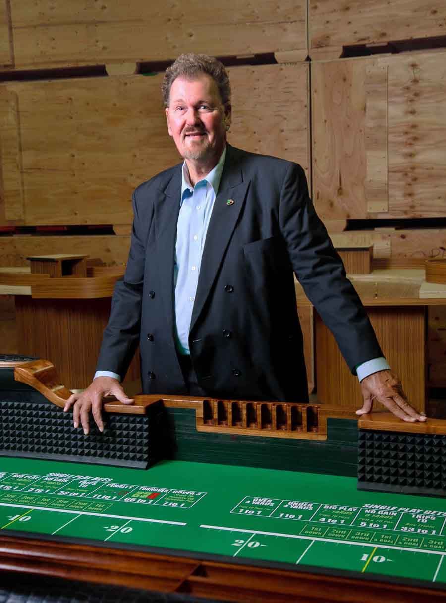 Man standing behind a green tabletop model in a wooden room, smiling with hands on the table