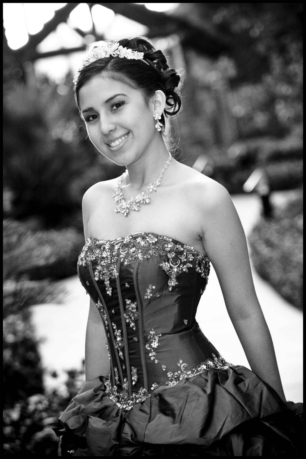 Smiling woman in a strapless formal dress posing outdoors on a garden path