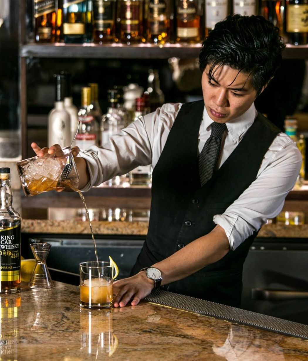 Bartender in a vest pours a cocktail at a bar with bottles lined behind him — Las Vegas commercial multi-family property photography