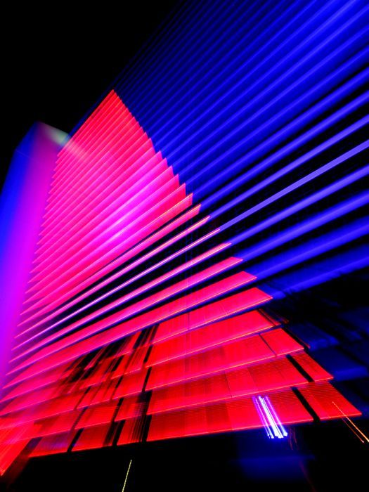 Neon-lit angular building with pink and blue diagonal light streaks against a dark sky — architectural photography