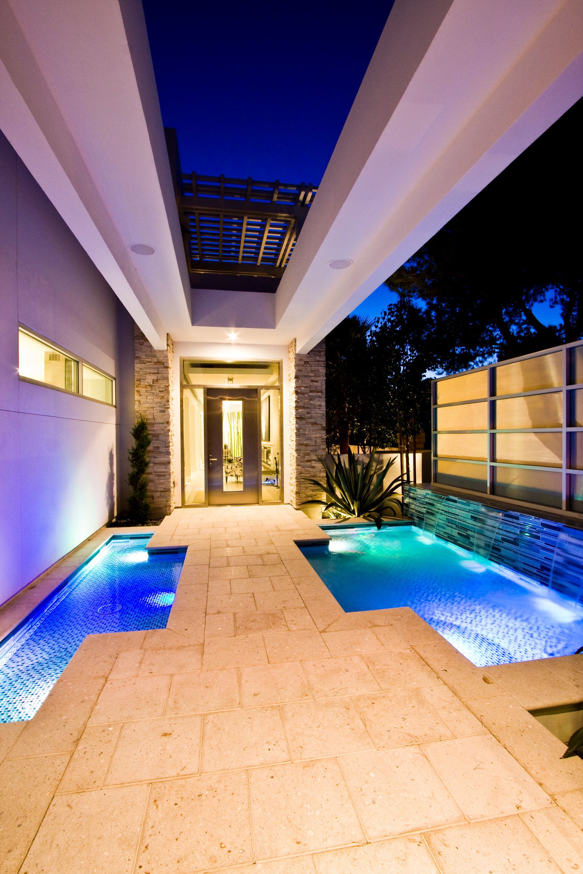 Modern house entryway with blue-lit side pools and a stone walkway at night — Las Vegas real estate photography