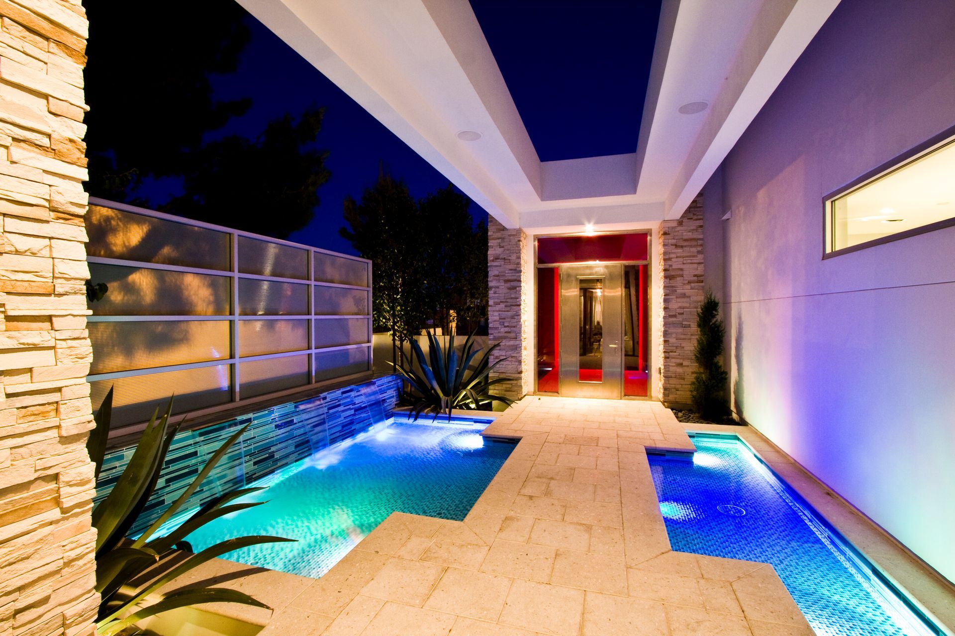 Modern courtyard with illuminated pool, stone walkway, and purple-lit walls at night — Las Vegas real estate photography