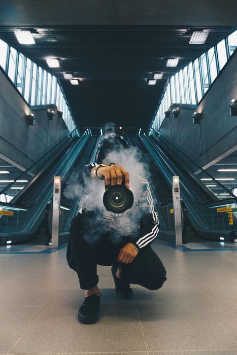 Person in a fluffy blue jacket crouches in a modern subway station, centered between escalators