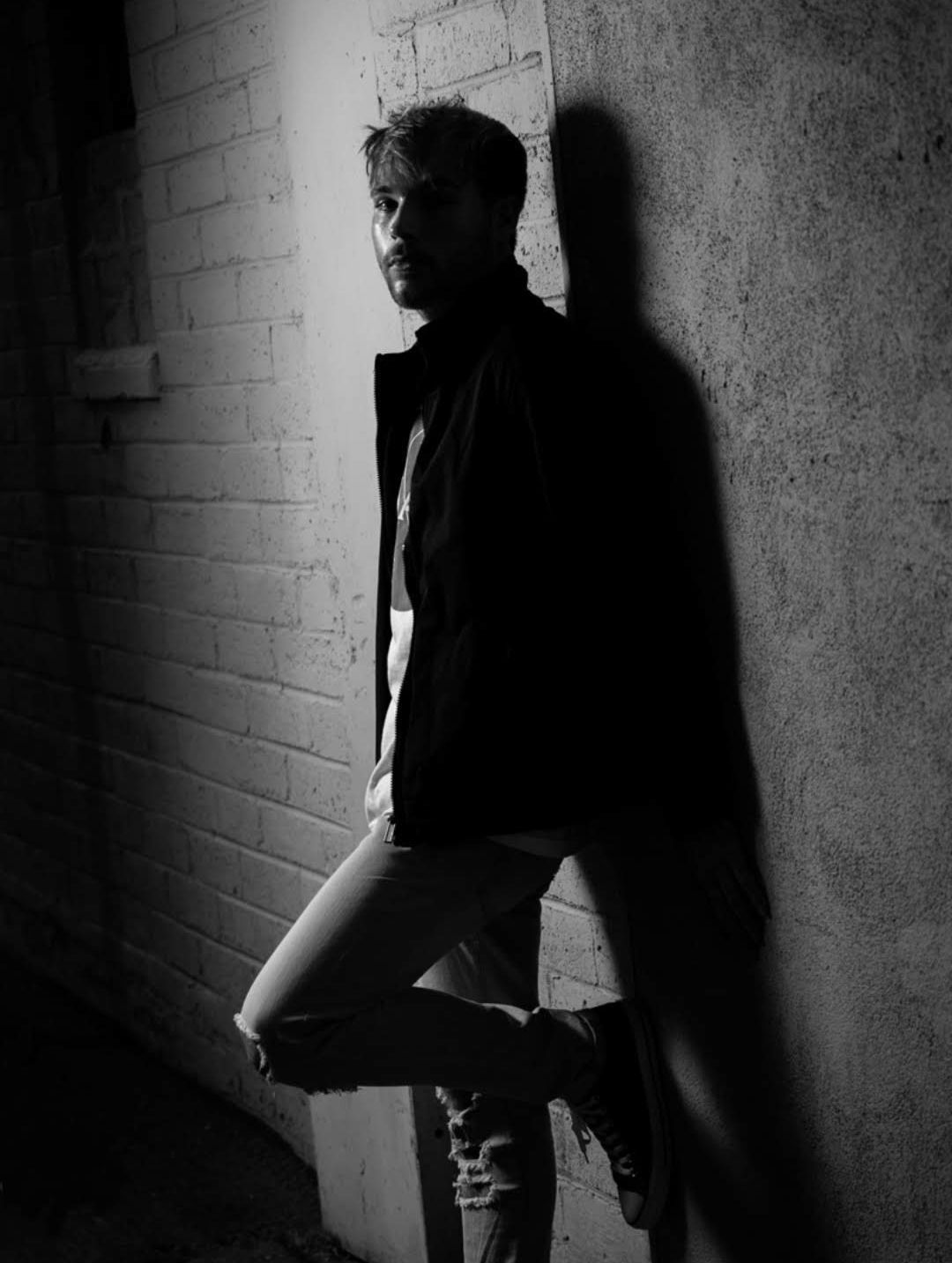 Black-and-white portrait of a person leaning against a brick wall in a dim alleyway — portrait photography