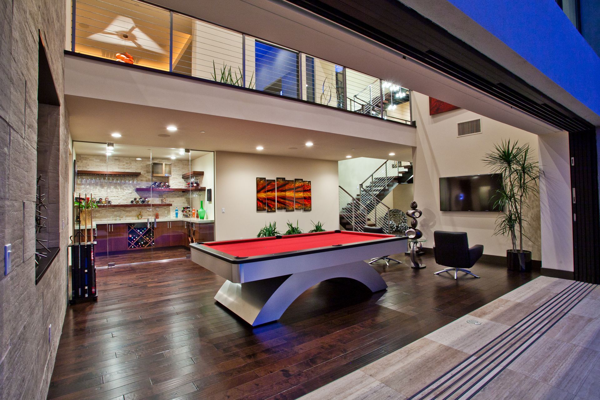 Modern open-plan game room with a red pool table, lounge chairs, kitchen, and staircase — Las Vegas real estate photography