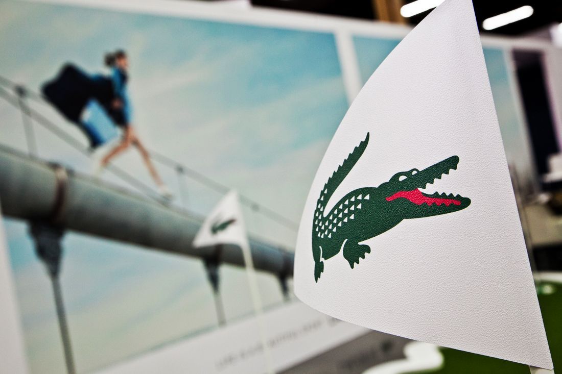 Lacoste crocodile logo on a white flag in front of a sports billboard — convention and event photography