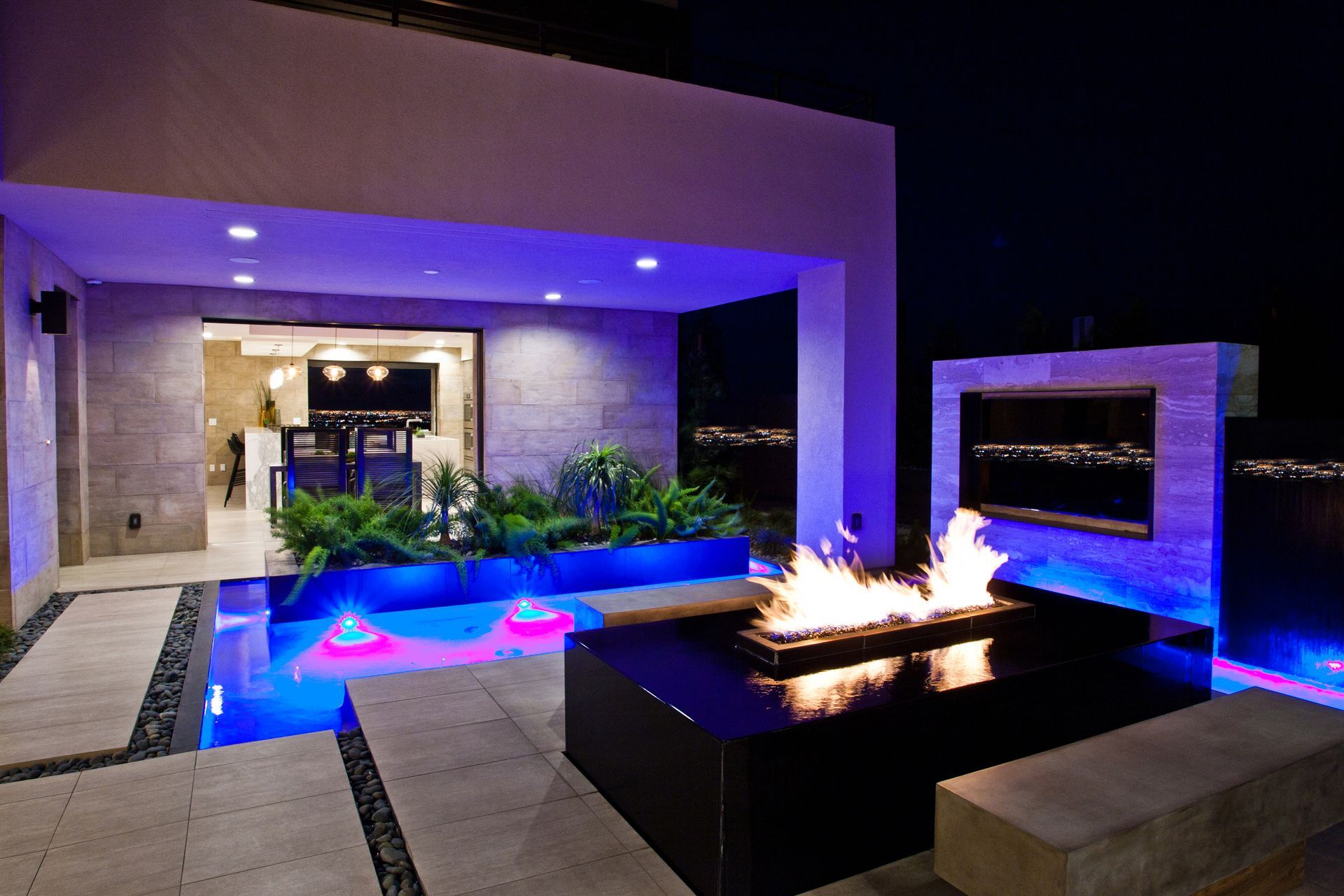 Modern patio with blue-lit pool, fire pit, and lounge seating outside a house at night — Las Vegas real estate photography