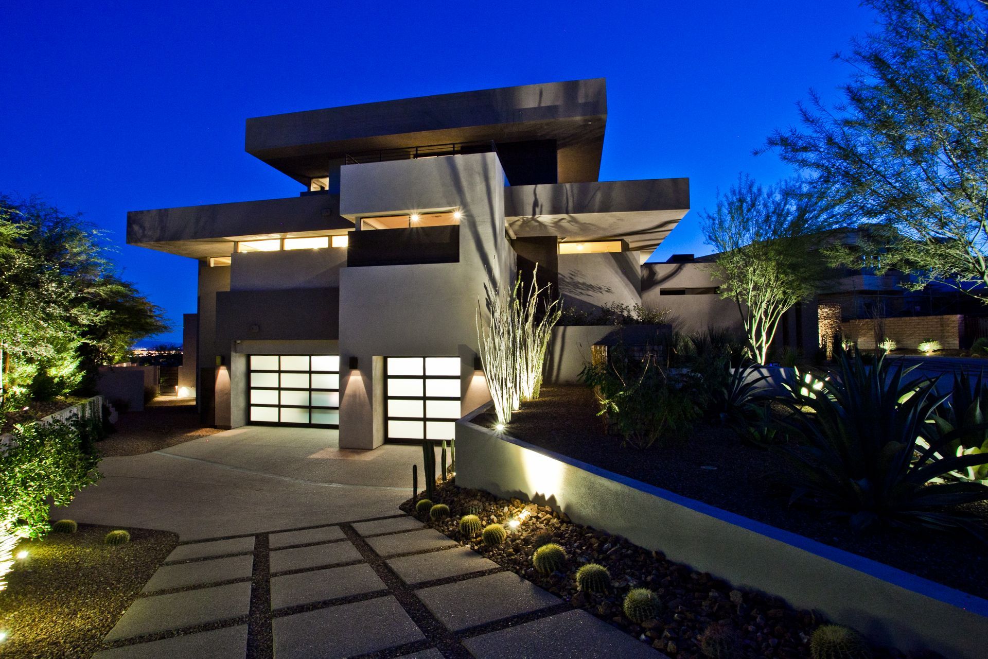 Modern house exterior at dusk with lit garage, stone path, and landscaped garden — Las Vegas real estate photography