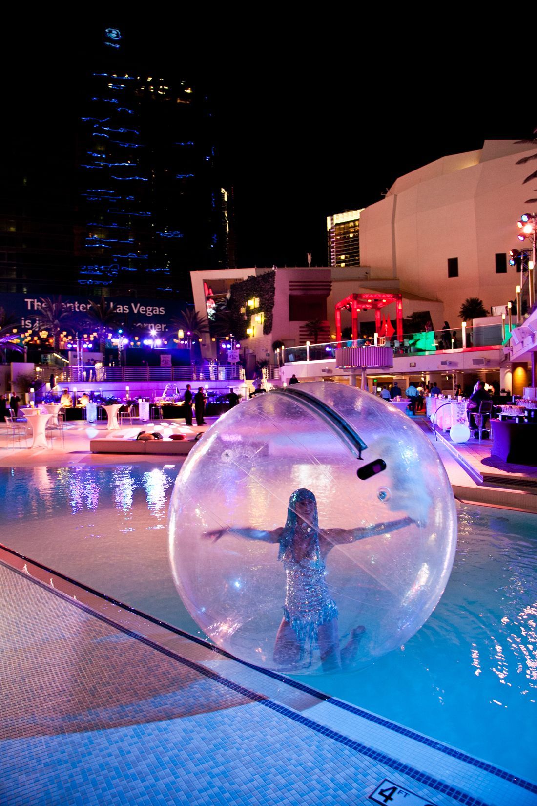 Person inside a transparent inflatable ball floating in a lit pool at night — event photography