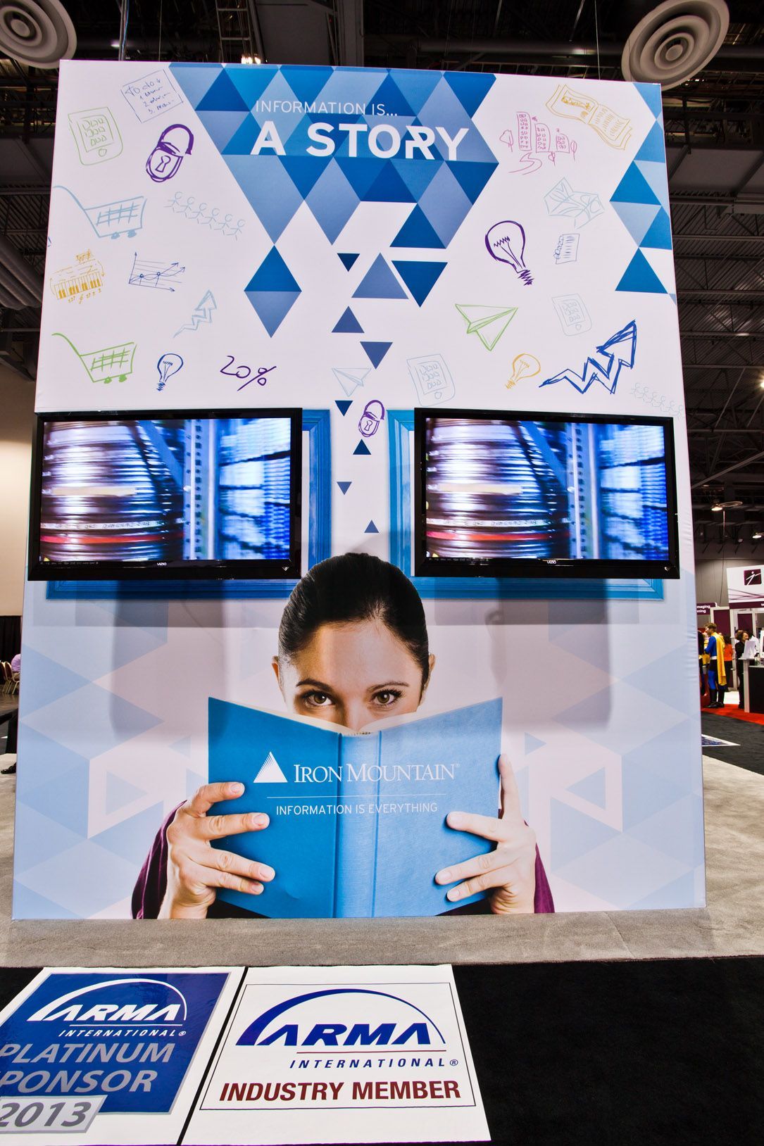 Trade show booth with blue-and-white geometric backdrop, dual screens — Las Vegas event photography