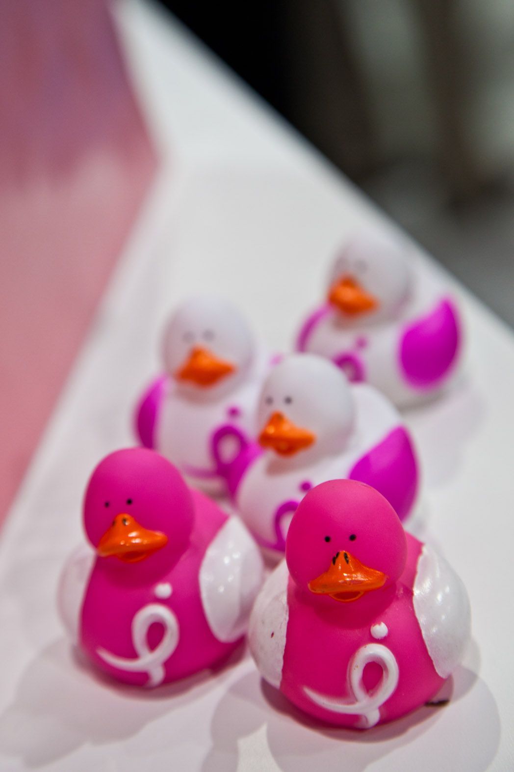 Pink and white rubber ducks with orange beaks on a white surface