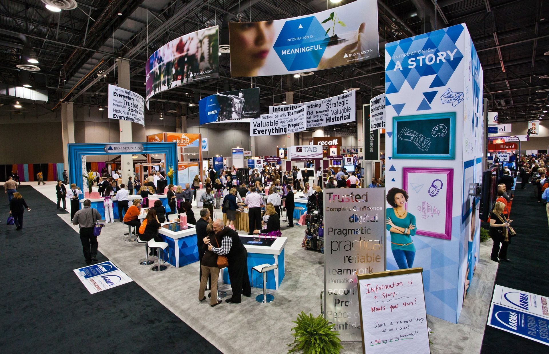 Crowded convention booth with blue-and-white displays and people browsing at a trade show — professional photography
