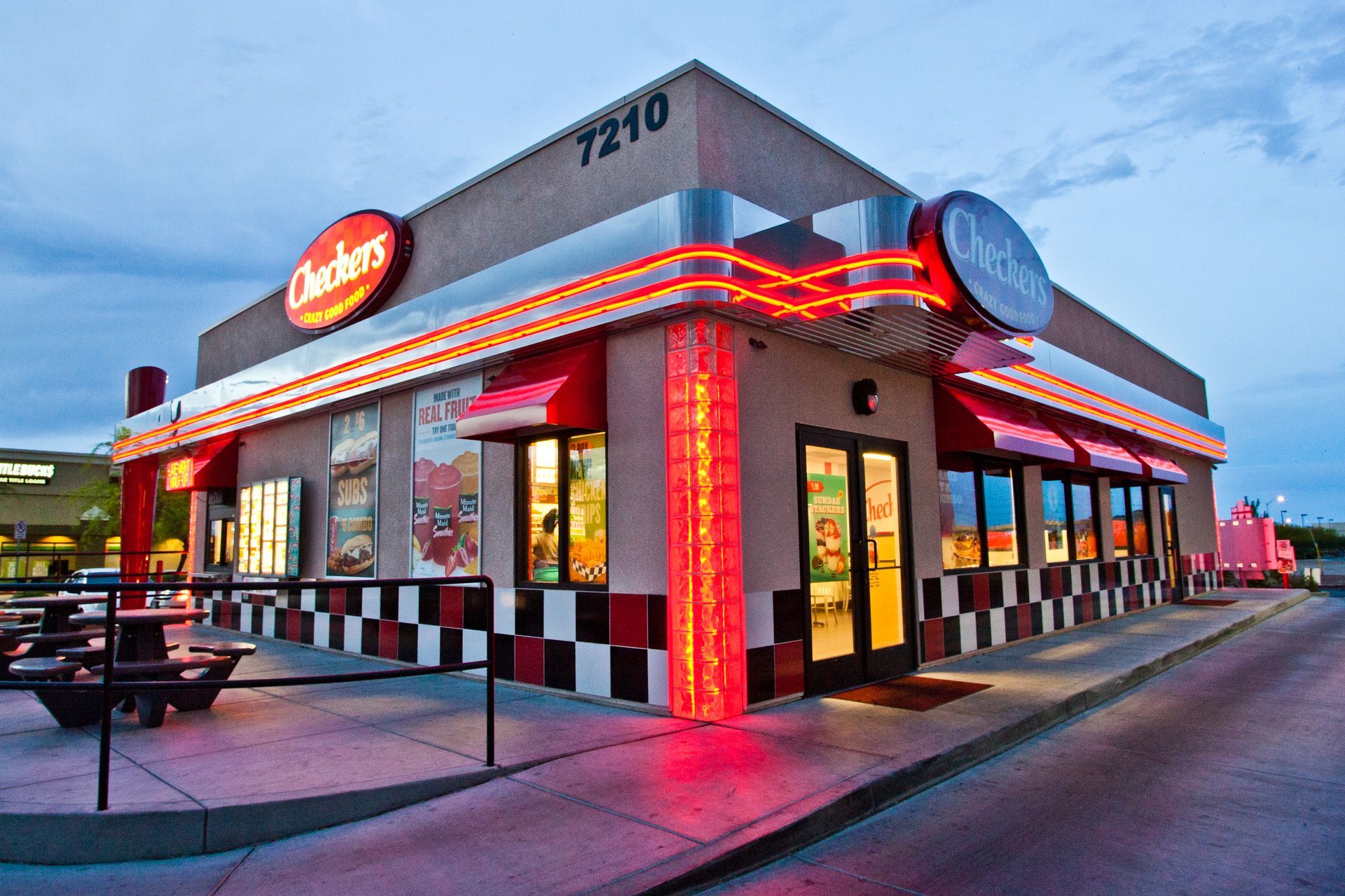 Neon-lit diner at dusk with red accents, checkerboard trim, and outdoor seating — commercial advertising photography