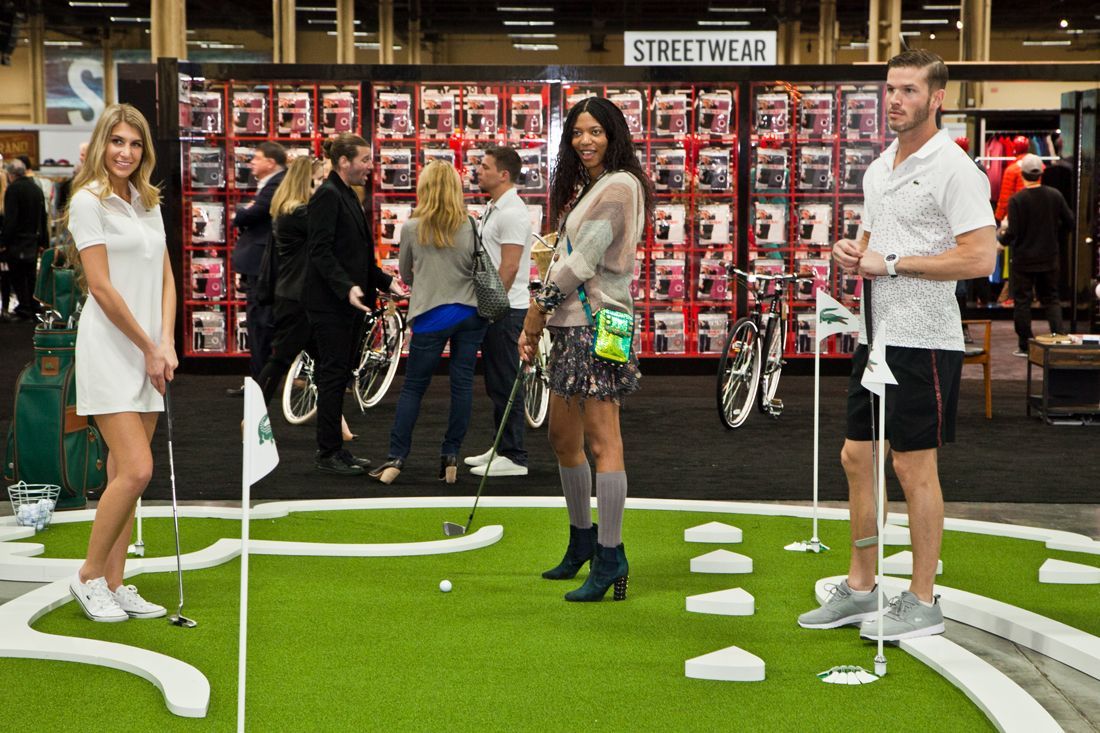 Group posing on an indoor mini-golf course with green turf and a display of bicycle wheels behind them
