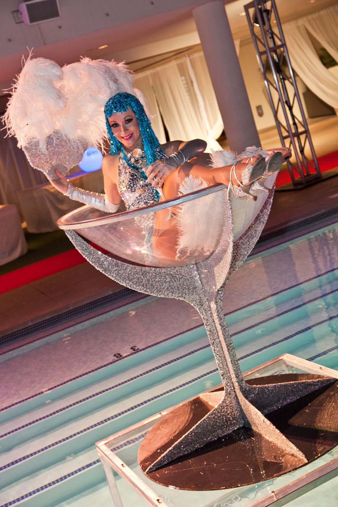 Blue-haired performer in a sparkling dress posing in a giant martini glass