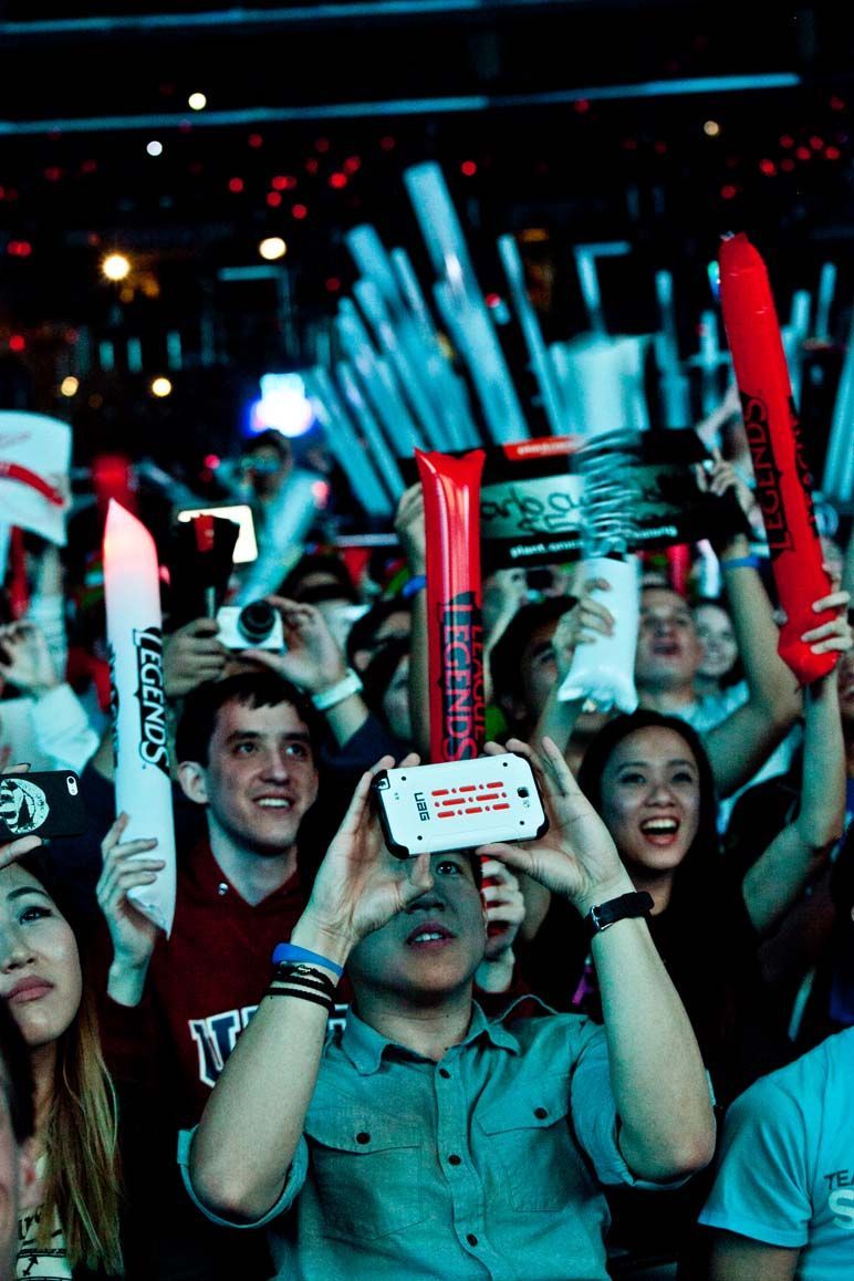 Crowd cheering at a concert, waving red and blue inflatable batons under stage lights