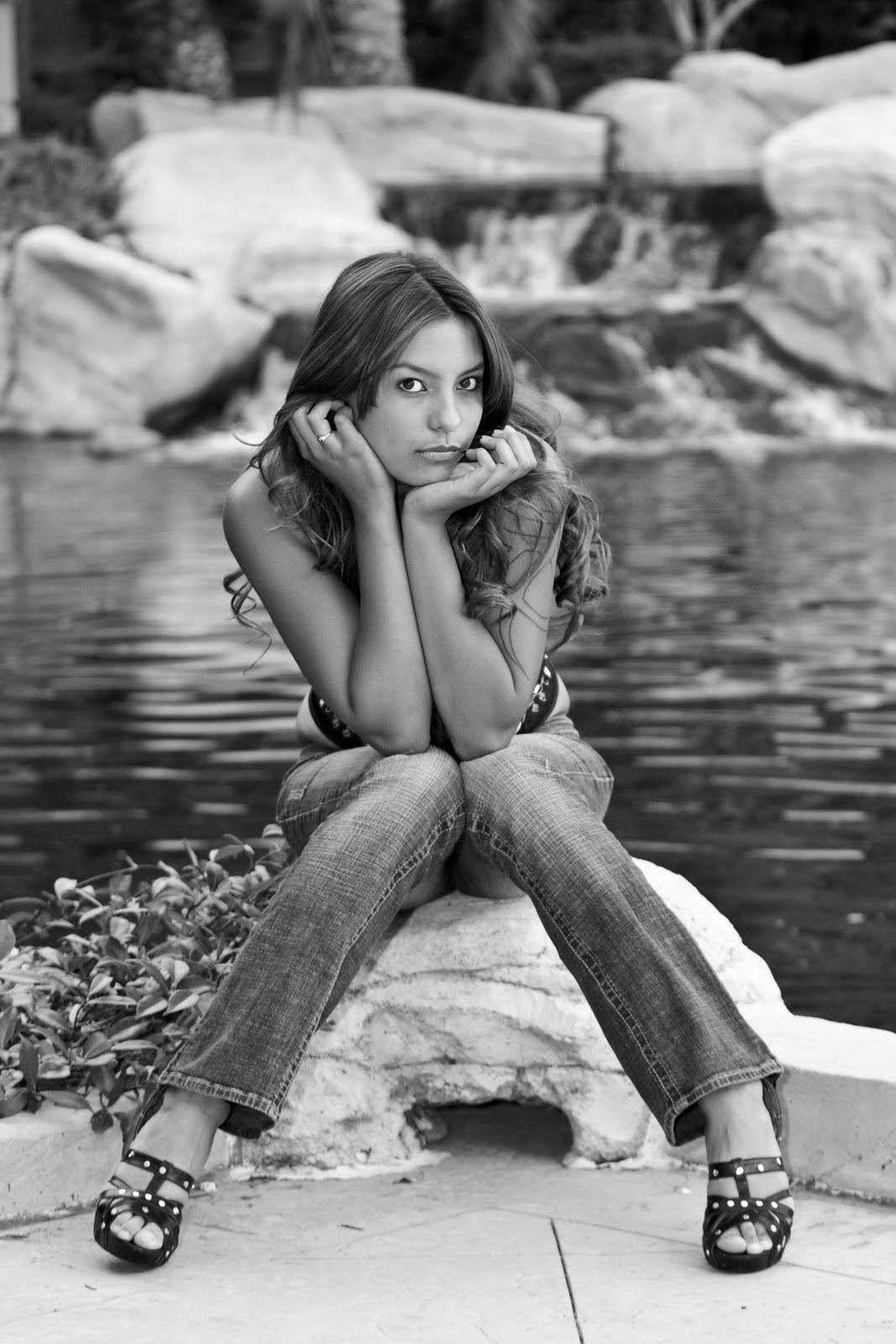 Person sitting on a rock by a pond, resting their chin on their hands, with water and stones behind