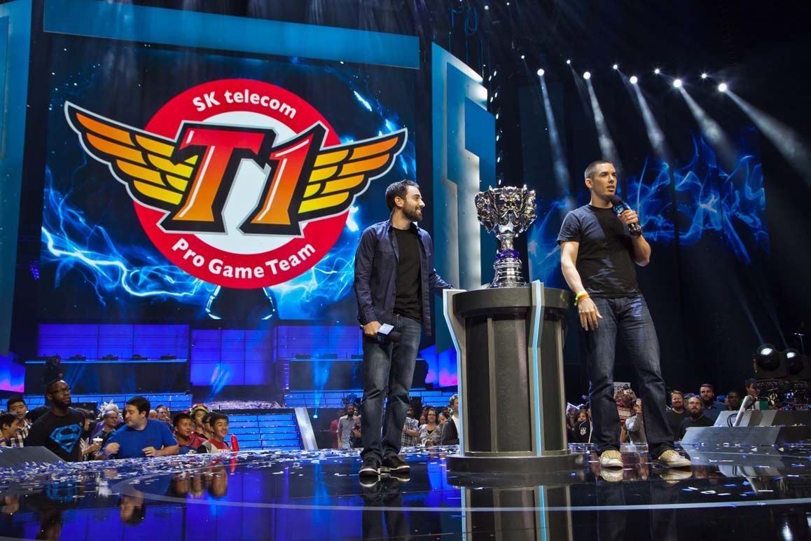 T1 esports stage with two presenters, a trophy on a podium, and a large winged logo on the screen — Las Vegas convention and event photography