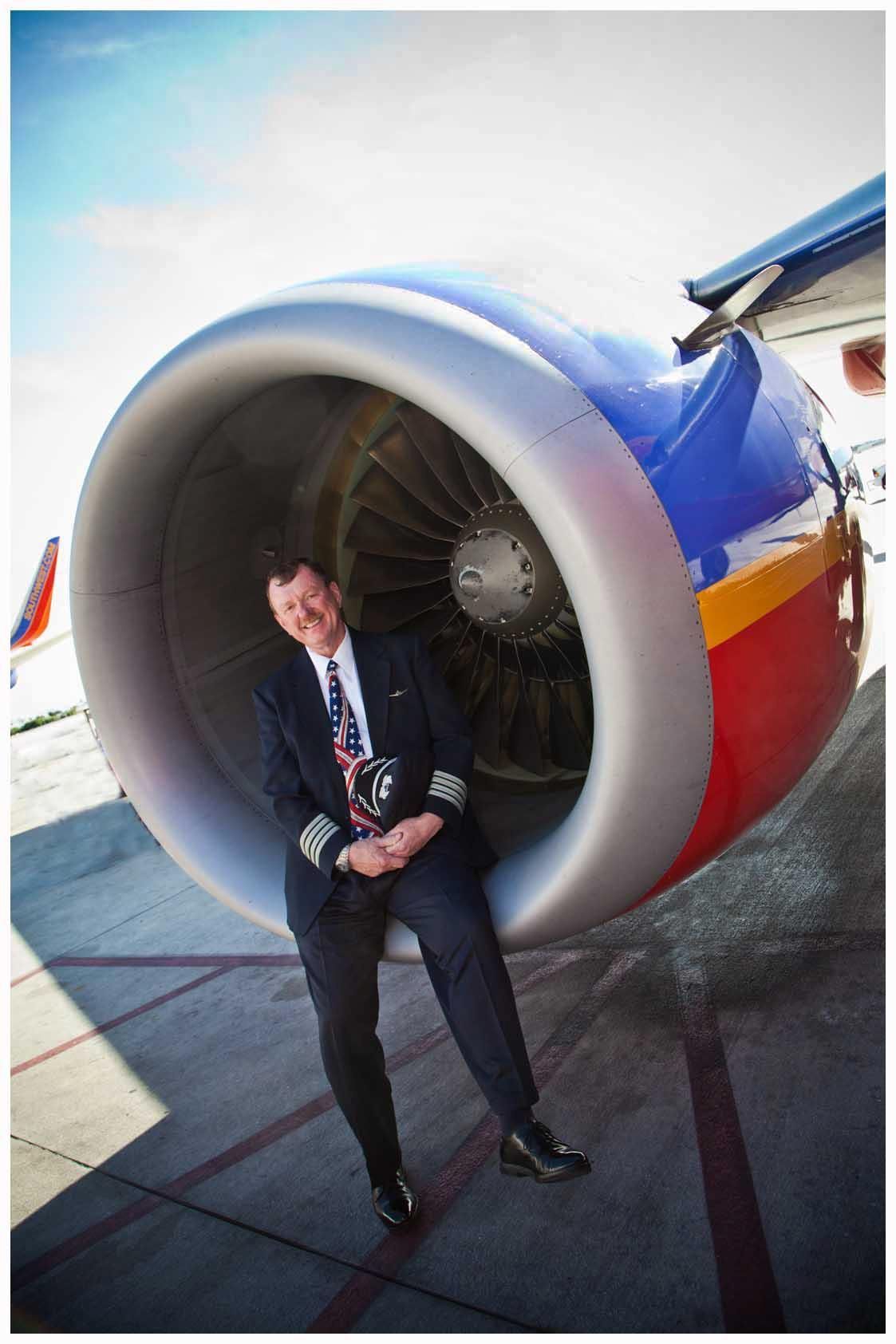 Person in a suit posing beside a large jet engine on an airport tarmac