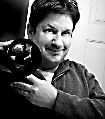 Black-and-white close-up of a person holding a shiny vinyl record, smiling at the camera