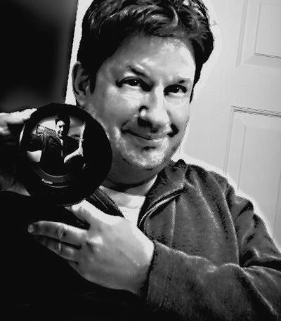 Man holding a black disc and smiling in a black-and-white selfie indoors