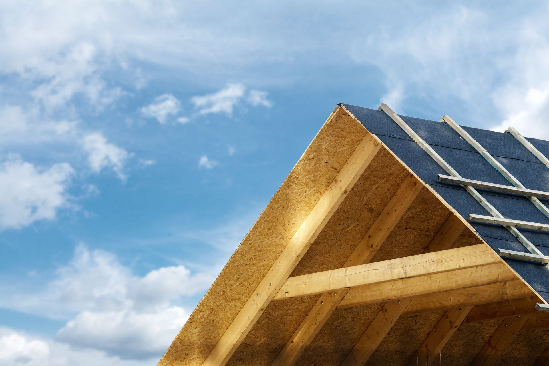 Wooden roof frame with solar panels against a blue, cloudy sky Wooden roof frame with solar panels against a blue, cloudy sky