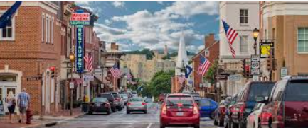 Busy small-town street with parked cars, storefronts, and American flags under a cloudy sky Busy small-town street with parked cars, storefronts, and American flags under a cloudy sky