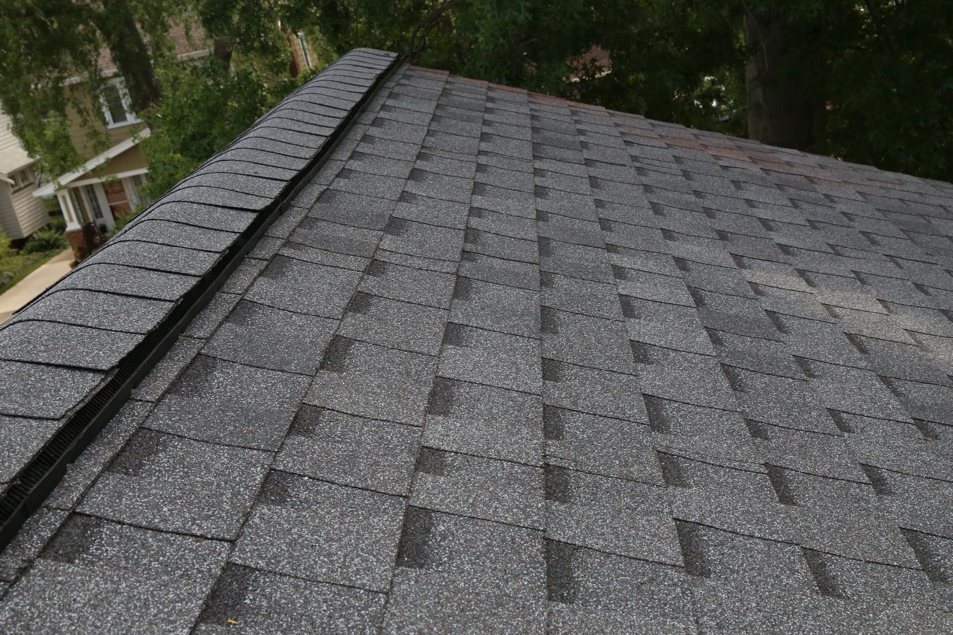 Close-up of a gray asphalt shingle roof on a house with dark flashing along the edge.