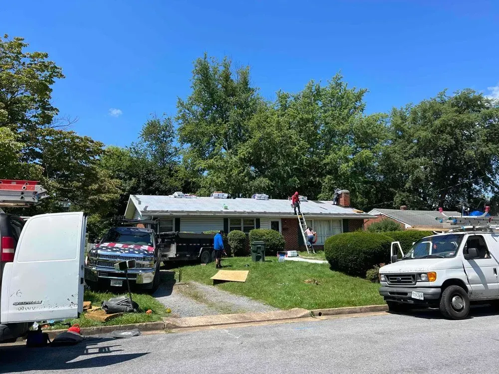 Single-story house with a front lawn, trees, and parked work trucks under a bright blue sky. Single-story house with a front lawn, trees, and parked work trucks under a bright blue sky.