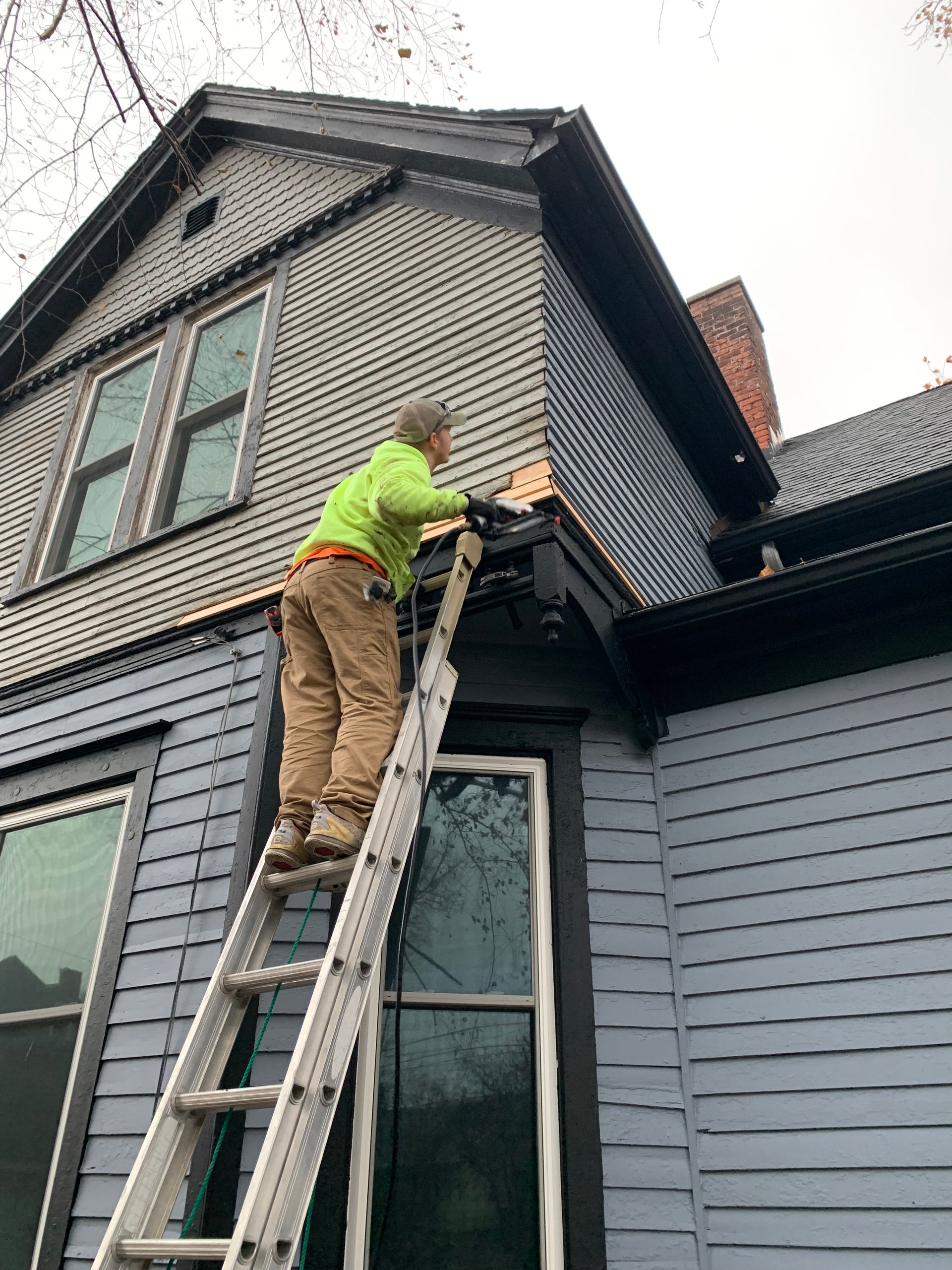A man is standing on a ladder painting the roof of a house.