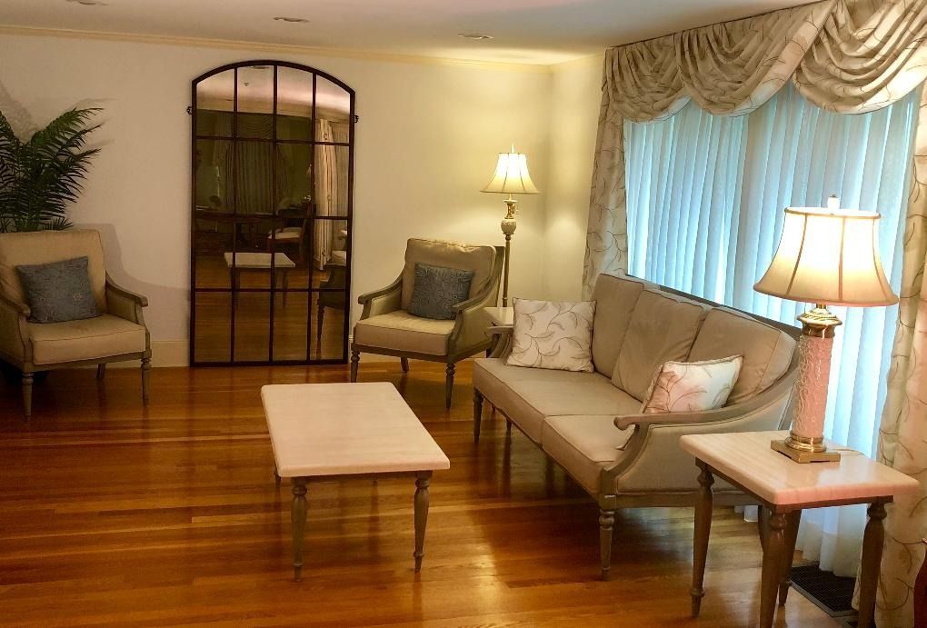 Elegant living room with sofa, chairs, coffee table, lamps, and large curtained window