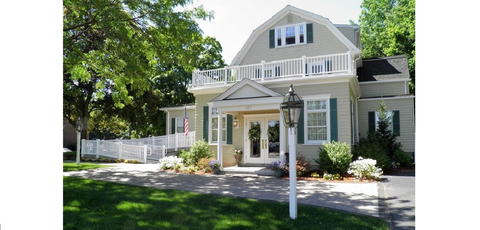 Light gray house with white trim, front porch, and manicured lawn on a sunny day