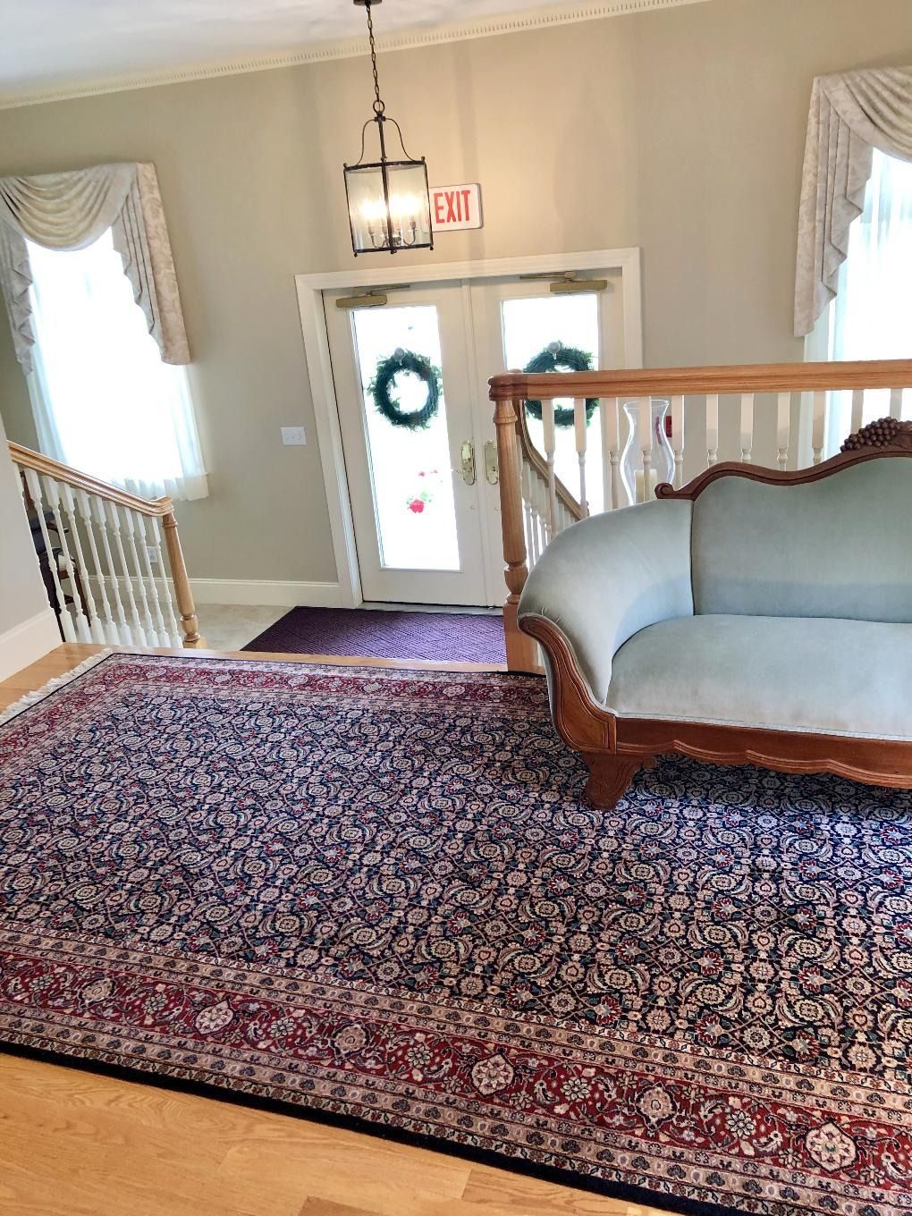 Hotel lobby landing with patterned red rug, blue loveseat, and double doors with wreath