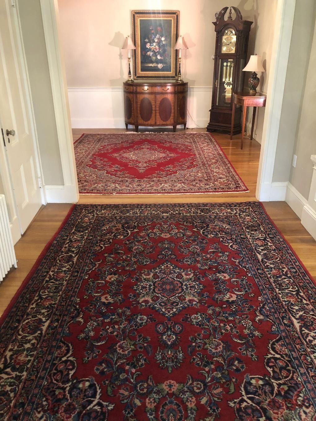 Hallway with red patterned rugs, a wooden cabinet with framed art, and a tall grandfather clock