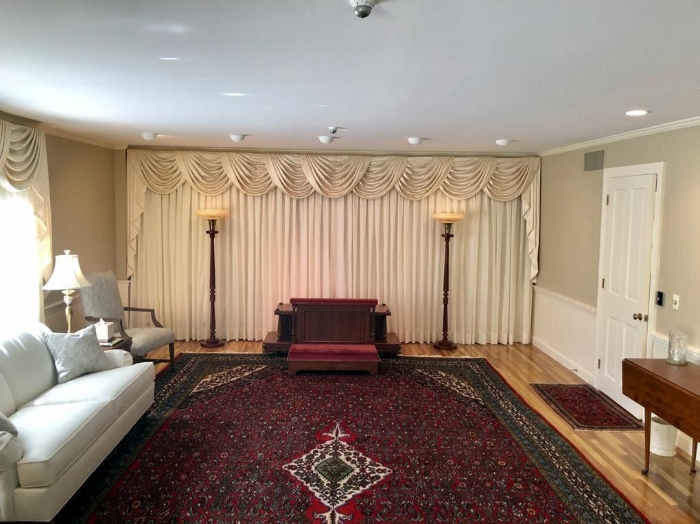 Empty living room with red rug, white sofa, curtains, and a small wooden stage centered on the far wall