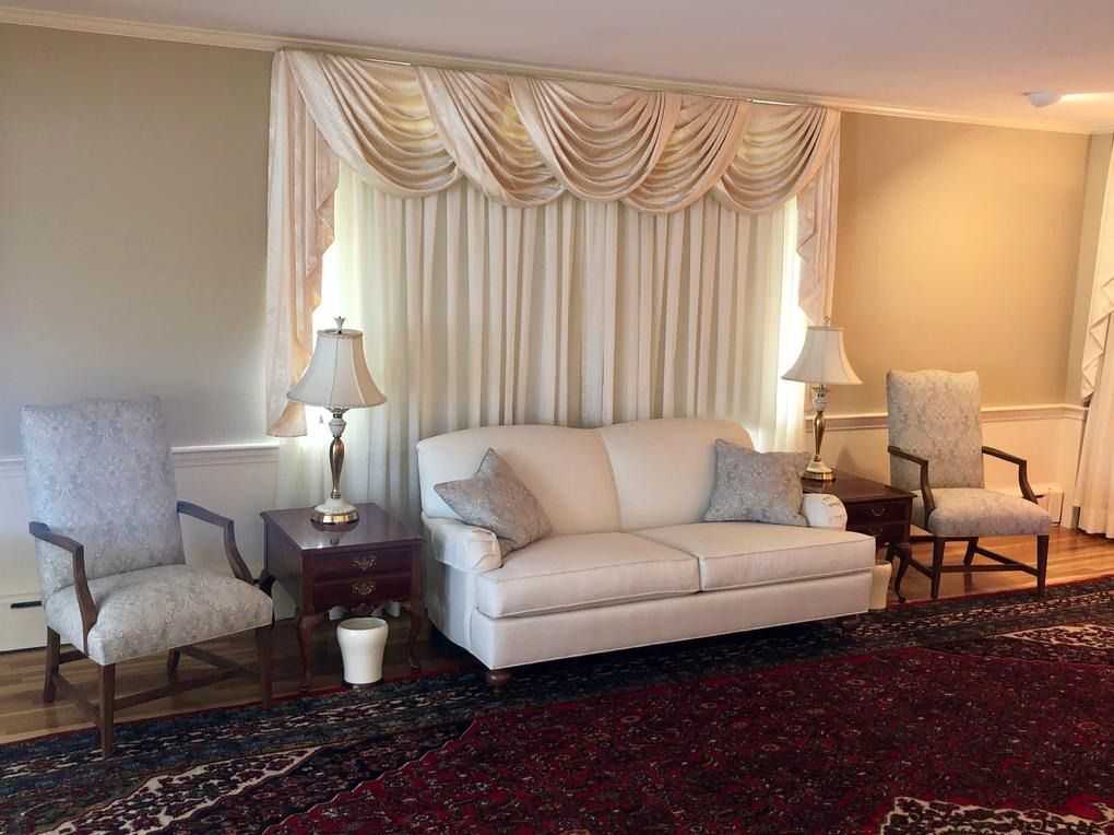 Elegant living room with beige sofa, two armchairs, lamps, and patterned rug under draped curtains