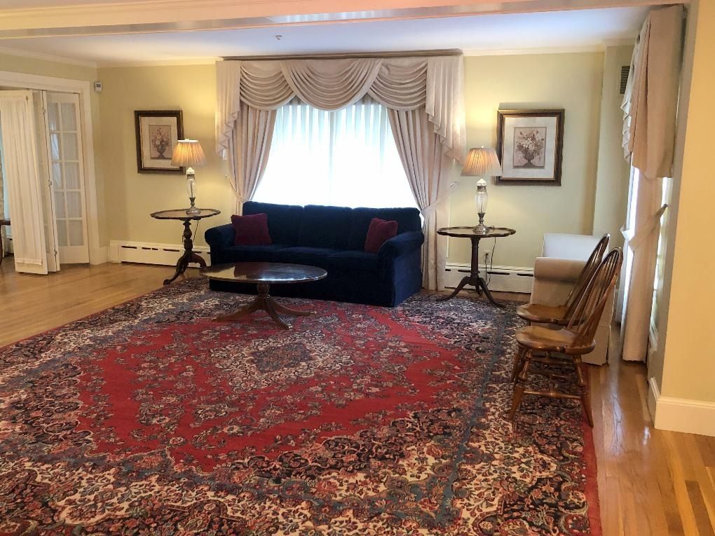 Elegant living room with red Persian rug, dark sofa, side tables, and draped bay window.
