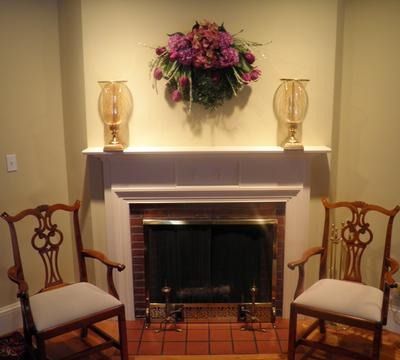 Elegant fireplace with floral arrangement, gold lamps, and two wooden chairs in a cozy living room