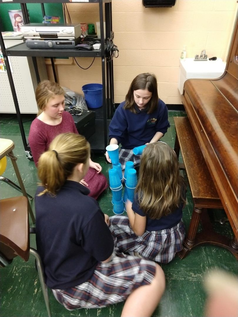 A group of young girls are sitting on the floor playing with blue cups